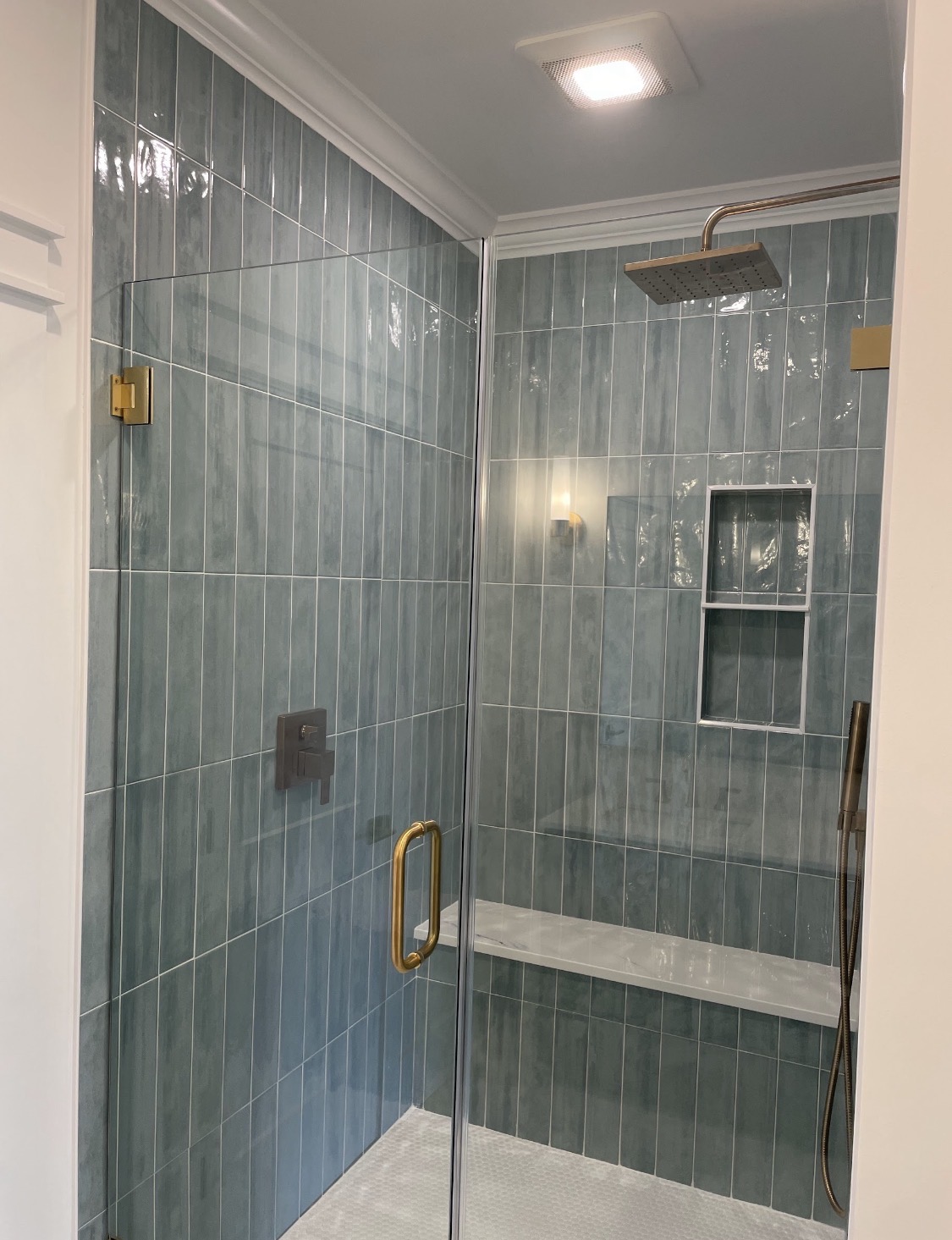 Glass-enclosed shower with brass hardware and tiled bench