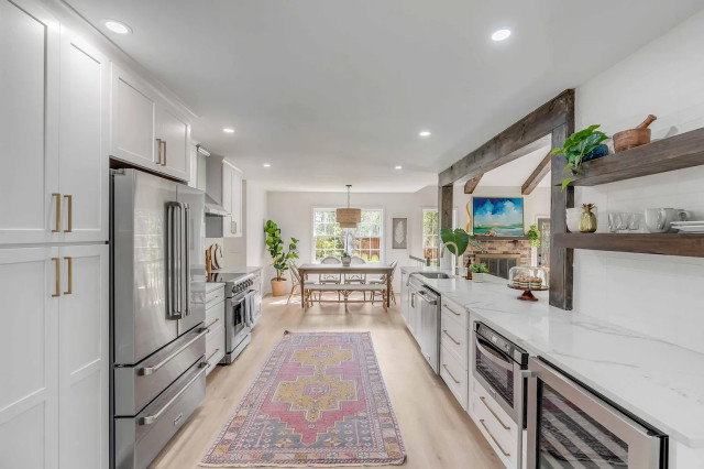 Kitchen aisle with brass hardware, floating shelves, and dining area beyond