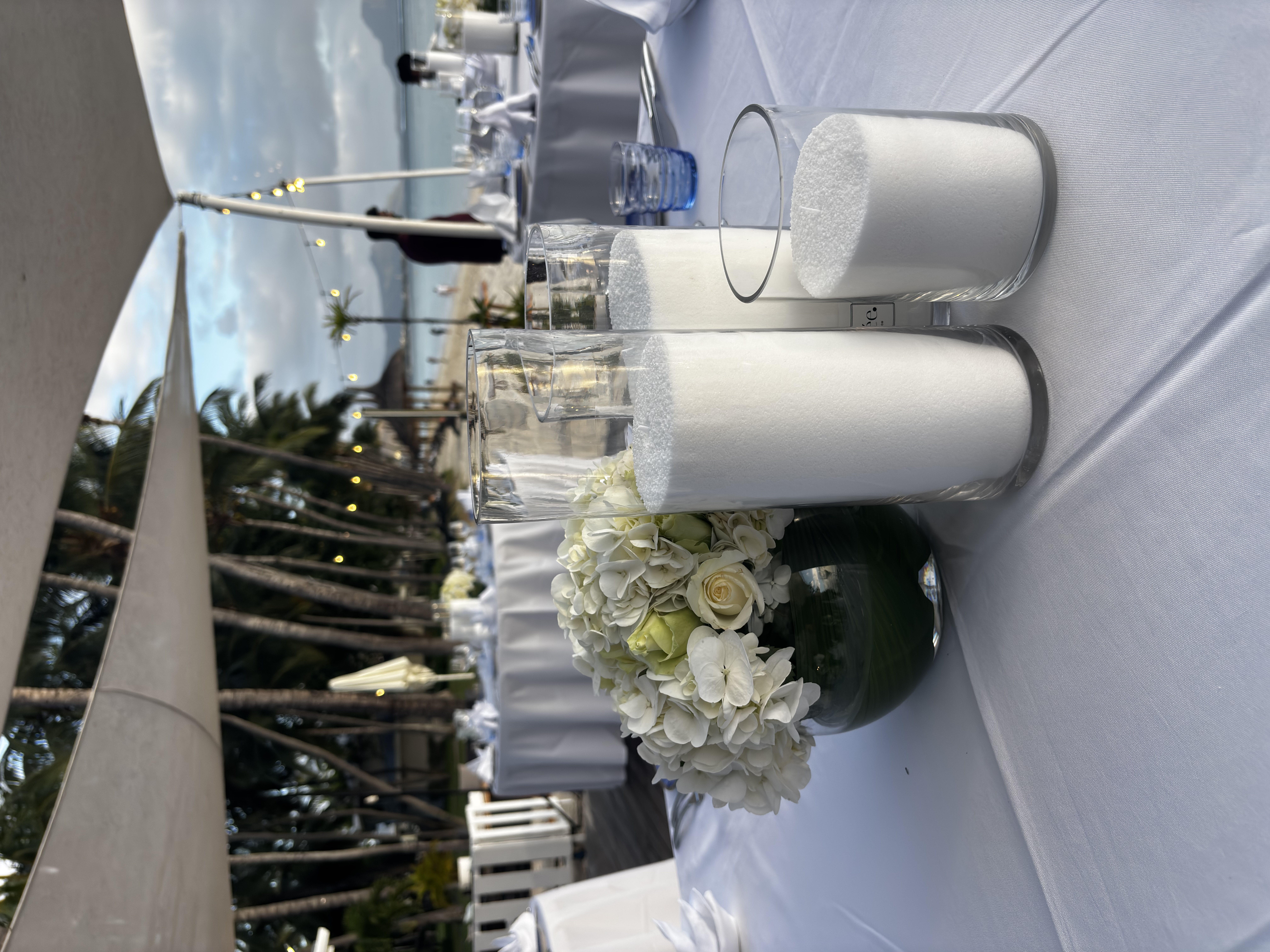 Composition florale blanche avec photophores cylindriques sur table de mariage en extérieur