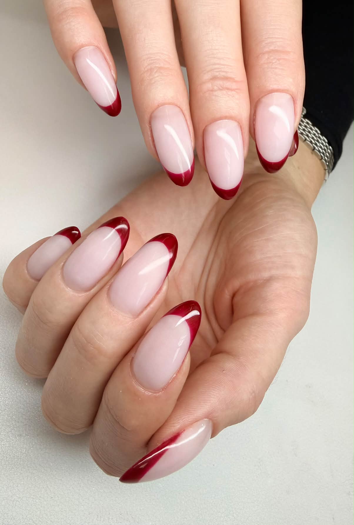 Pale pink almond nails with glossy burgundy French tips