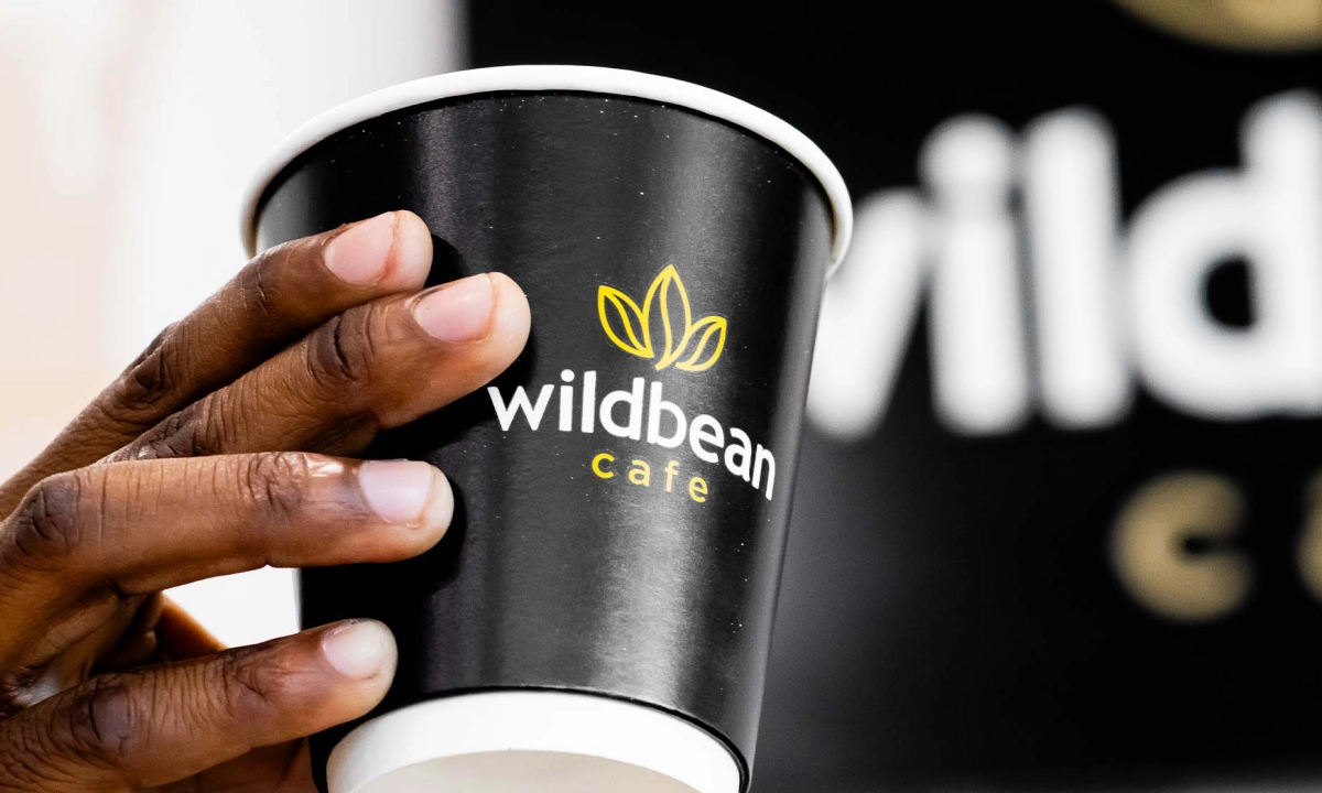 Hand holding a black Wildbean Cafe disposable coffee cup with branding.
