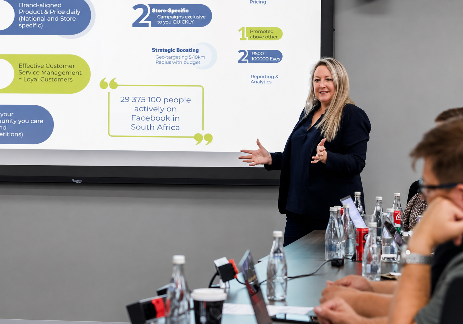 Supermarketing presenter in a dark blazer addressing a franchise marketing meeting, with a projection screen behind her showing retail marketing insights including Facebook audience reach figures for South Africa.