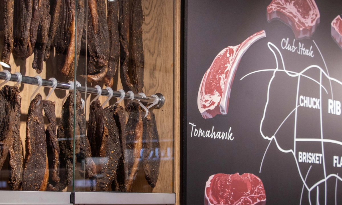 Deli display cabinet featuring hanging biltong next to a meat cut diagram mural.