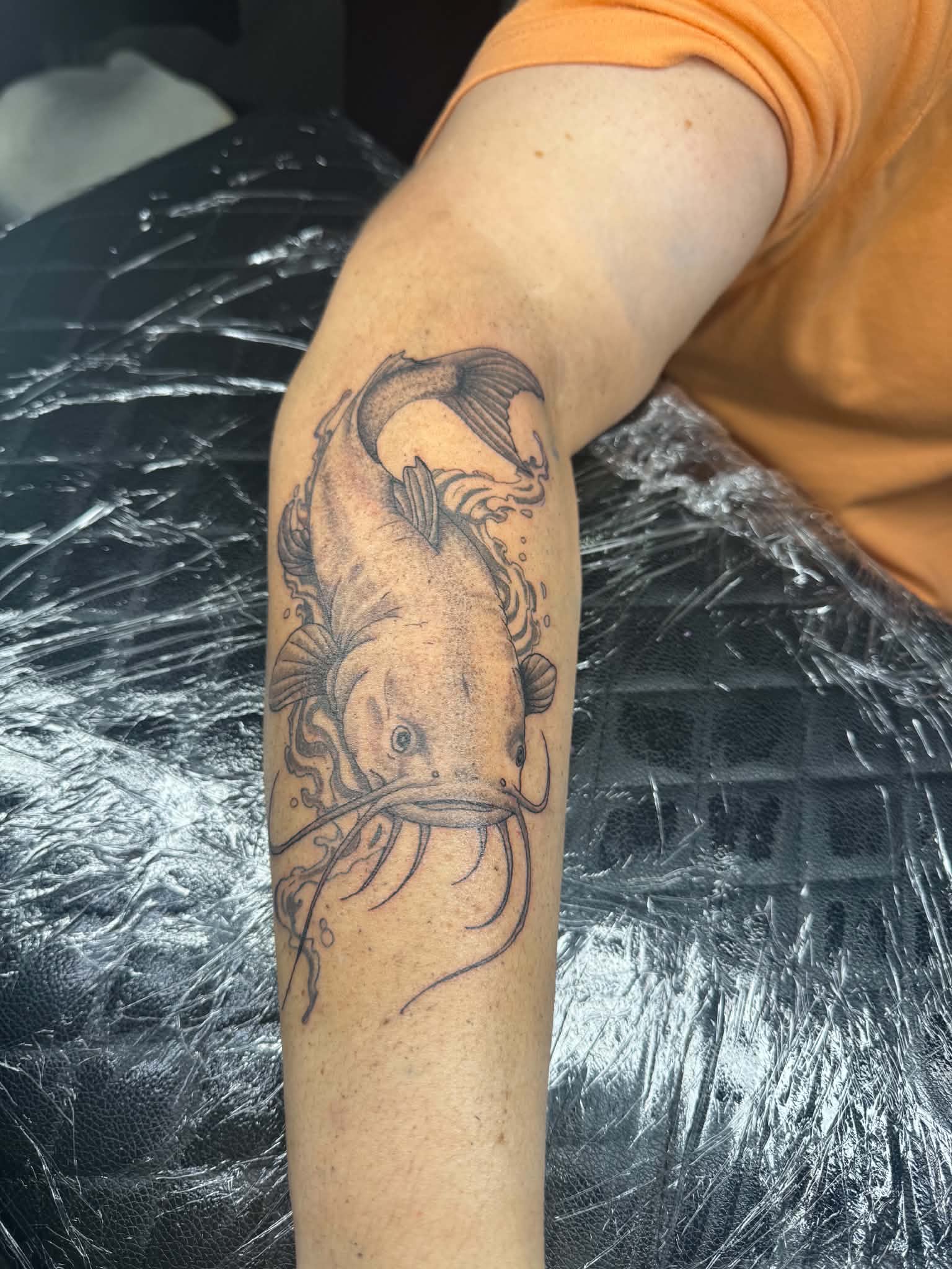 Catfish in flowing water forearm tattoo