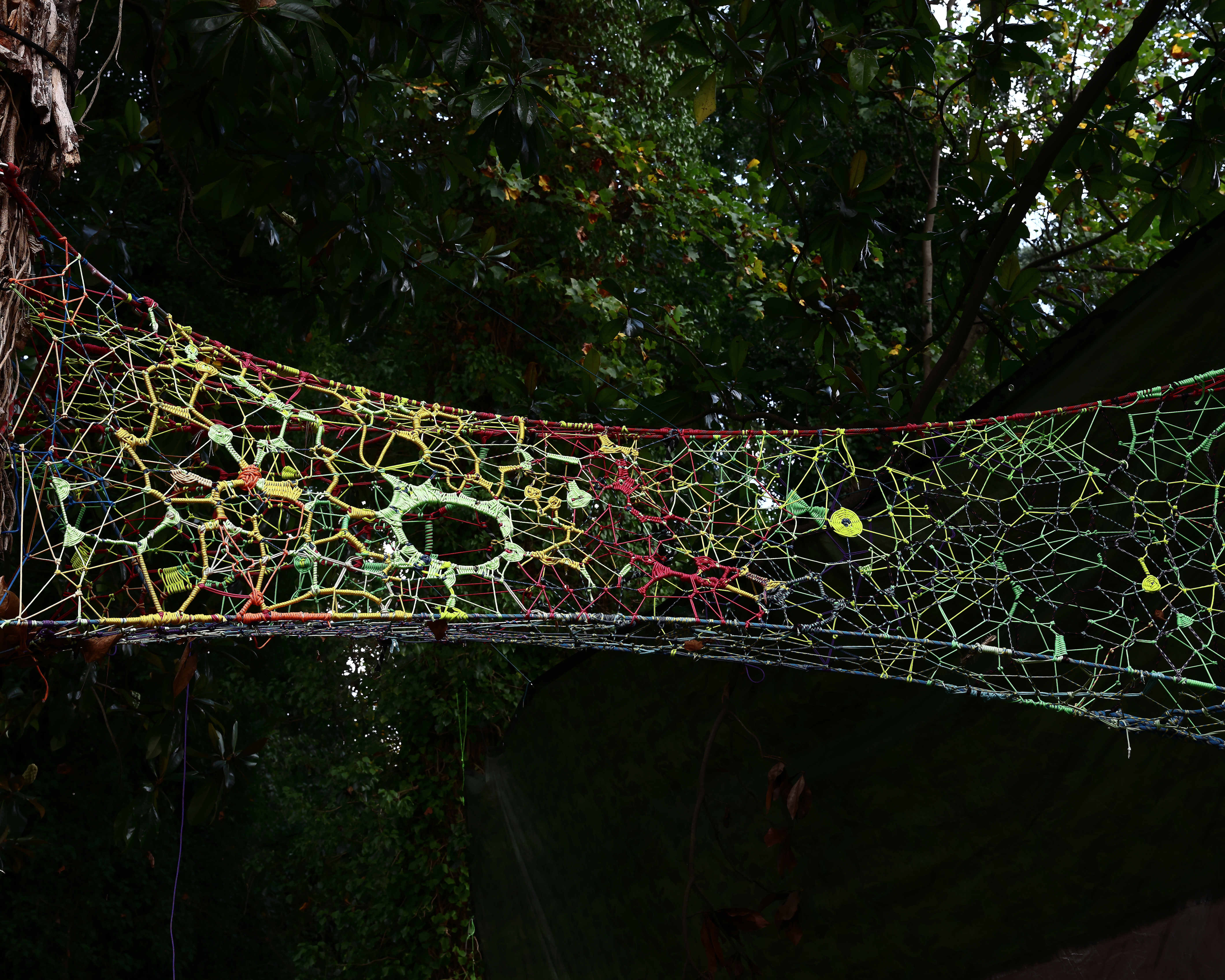 Colorful hand-woven tensioned web suspended between trees