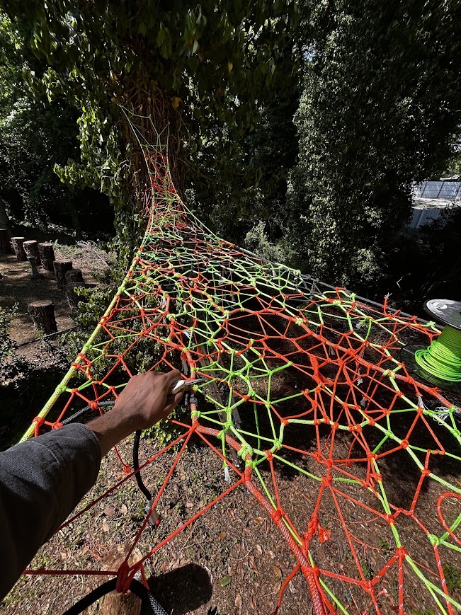 First-person view weaving a neon green and orange net among the trees