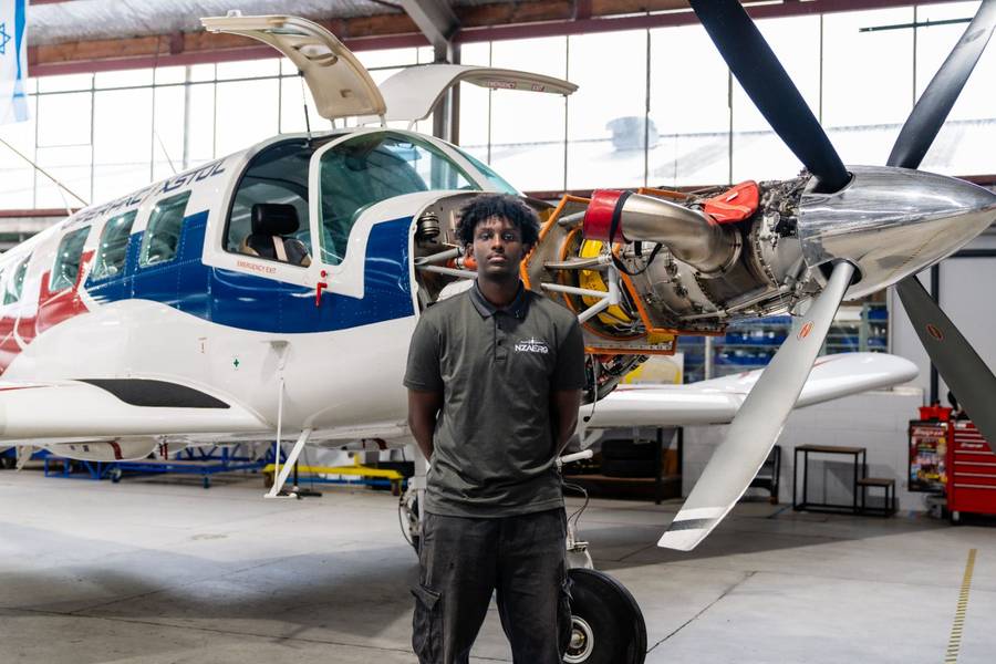 Young person standing in front of a single-engine aircraft in a manufacturing hangar