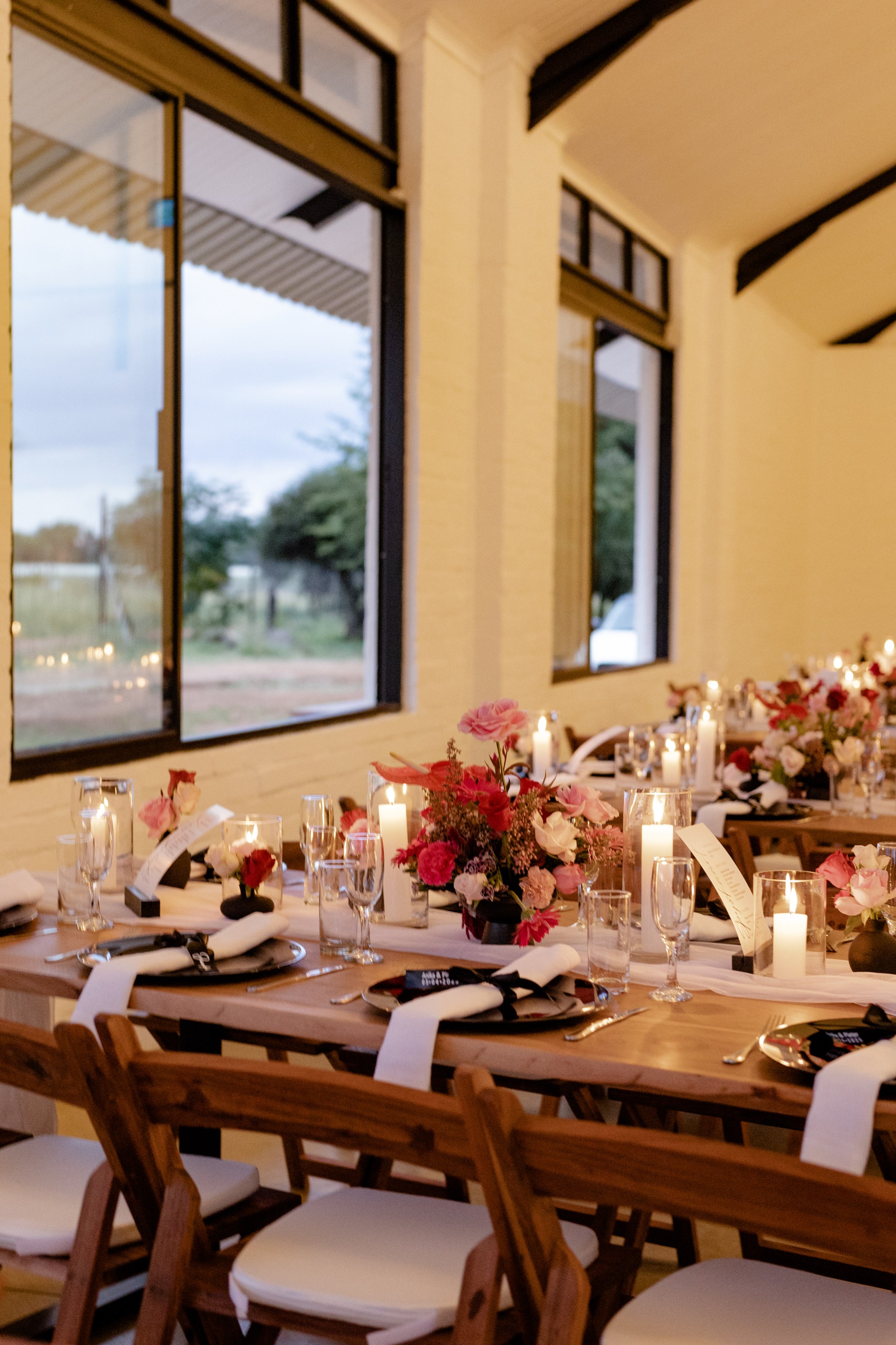 Long banquet table with floral runners, pillar candles and warm evening light