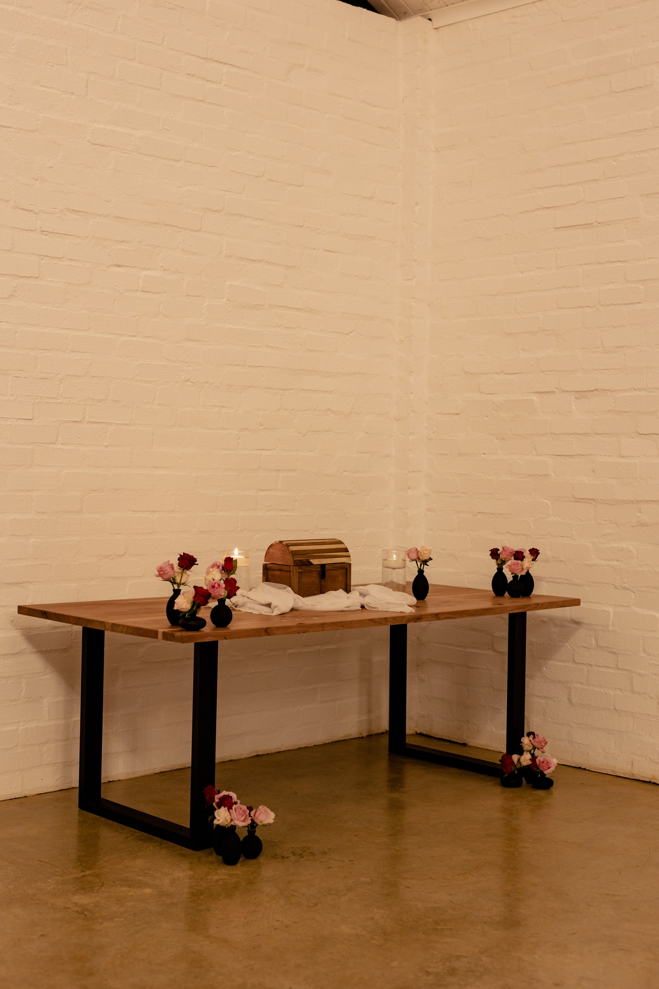 Gift table with wooden chest, bud vases and candlelight against white brick