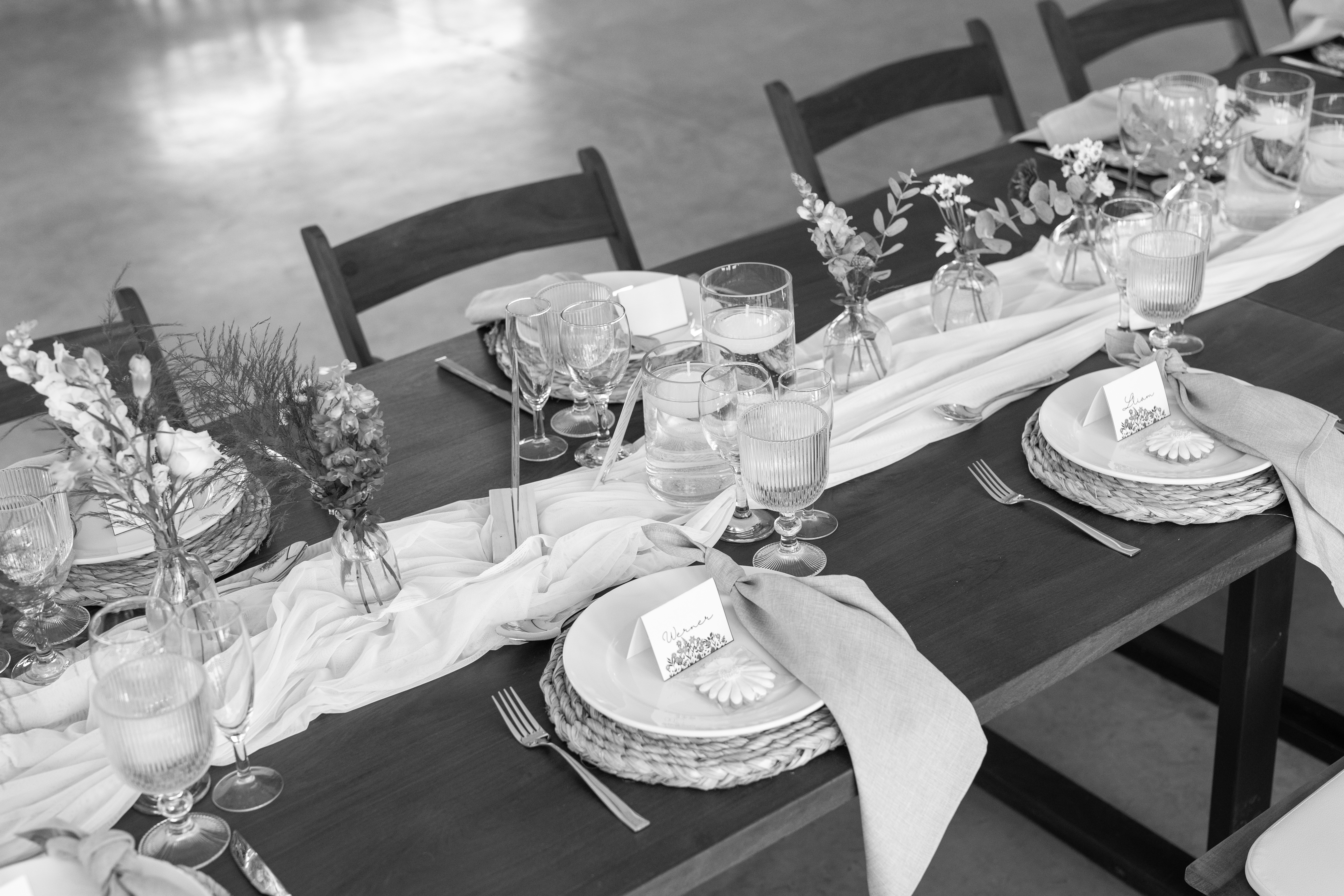 Black-and-white detail of place settings with woven placemats and flower-shaped favours
