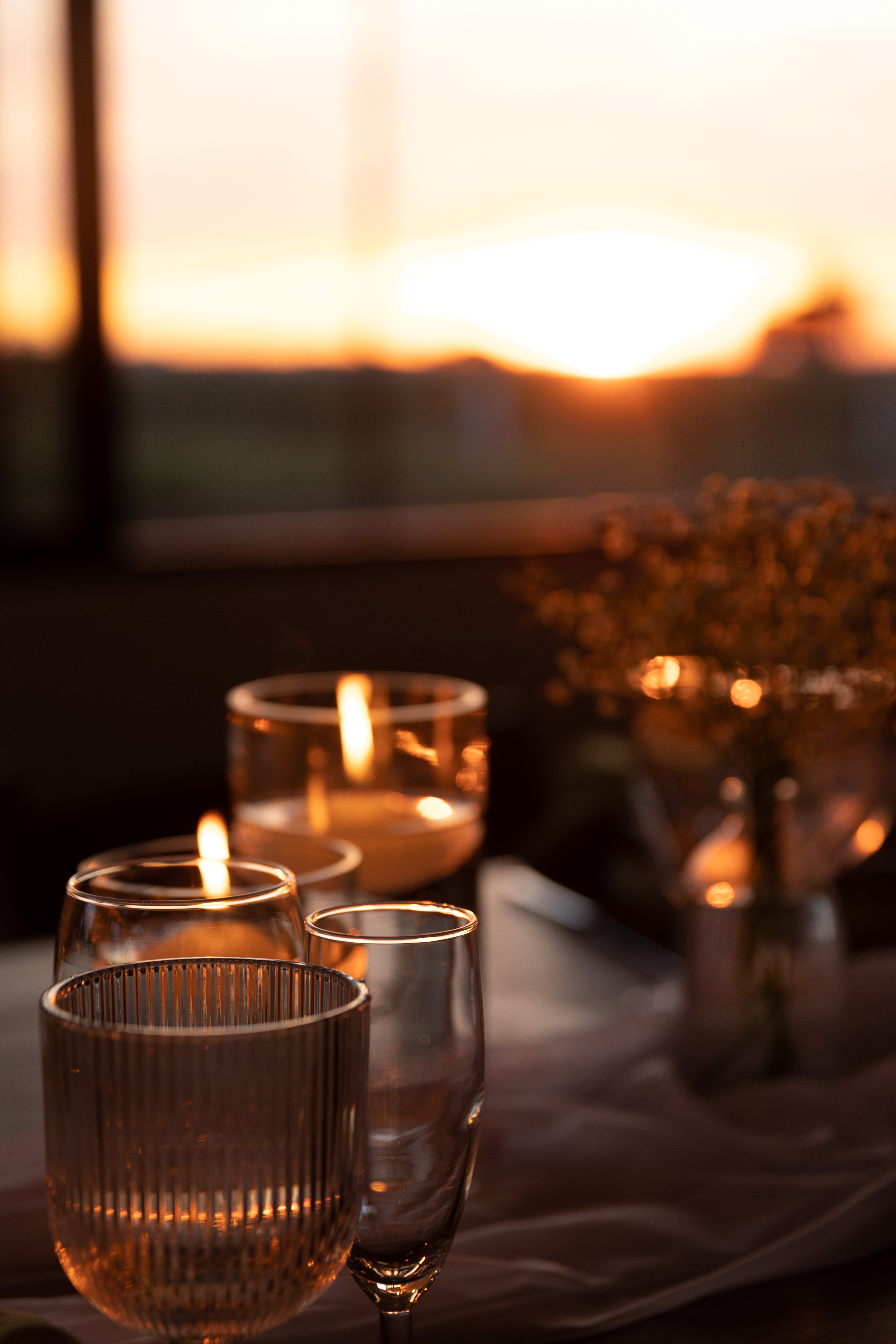 Glassware catching the warm sunset glow with dried flower sprigs and candlelight