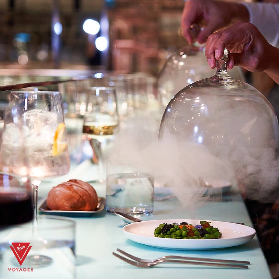 An elegant plated dish under a smoking glass cloche in a Virgin Voyages test kitchen