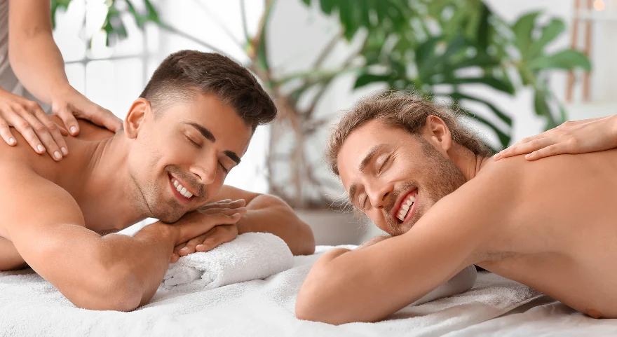 Two gay men smiling and relaxed side by side during a couples M4M massage session — gay massage for relaxation and better sleep