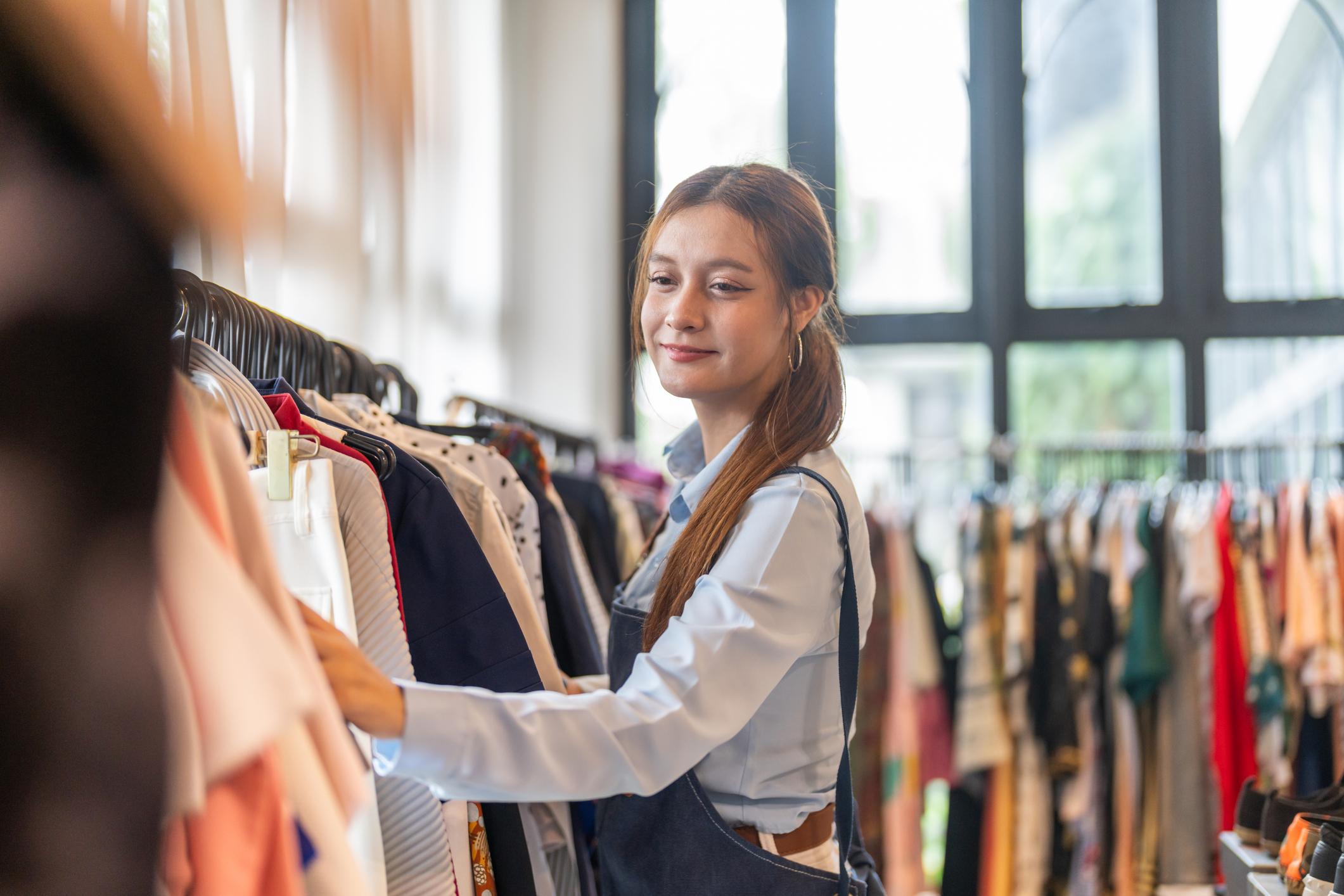 A boutique owner in an apron browsing clothing racks in her shop.
