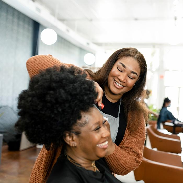 A hairstylist smiling while styling a client’s hair in a bright salon.