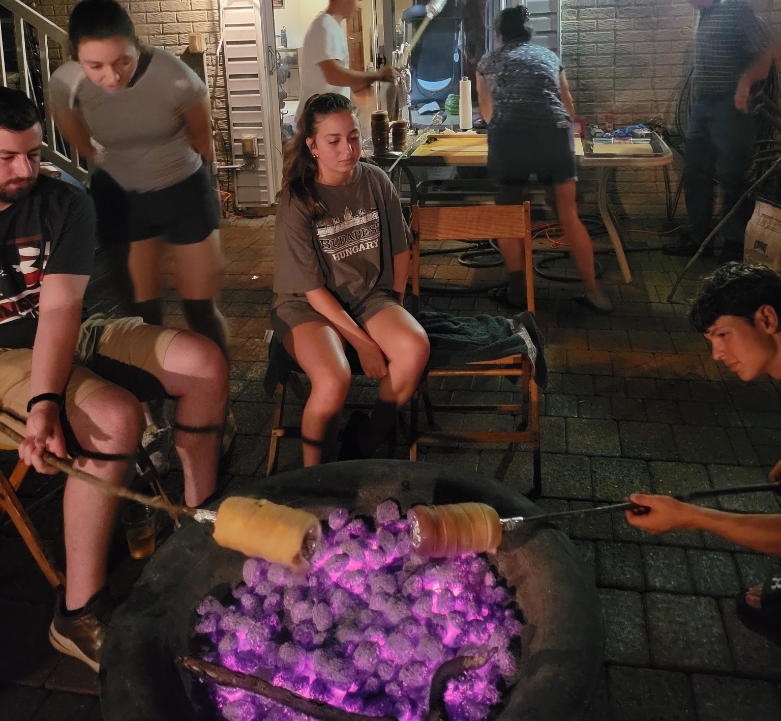 Family and friends roasting chimney cakes over an open fire pit