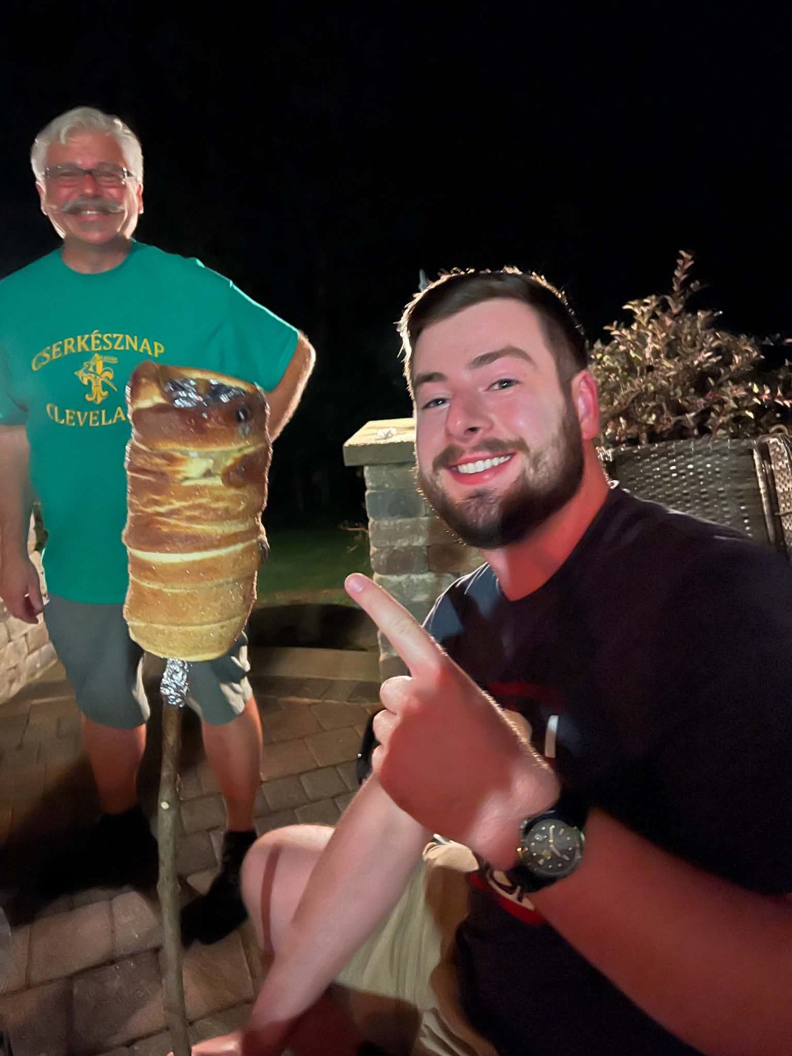 A finished golden chimney cake held up on a wooden stick