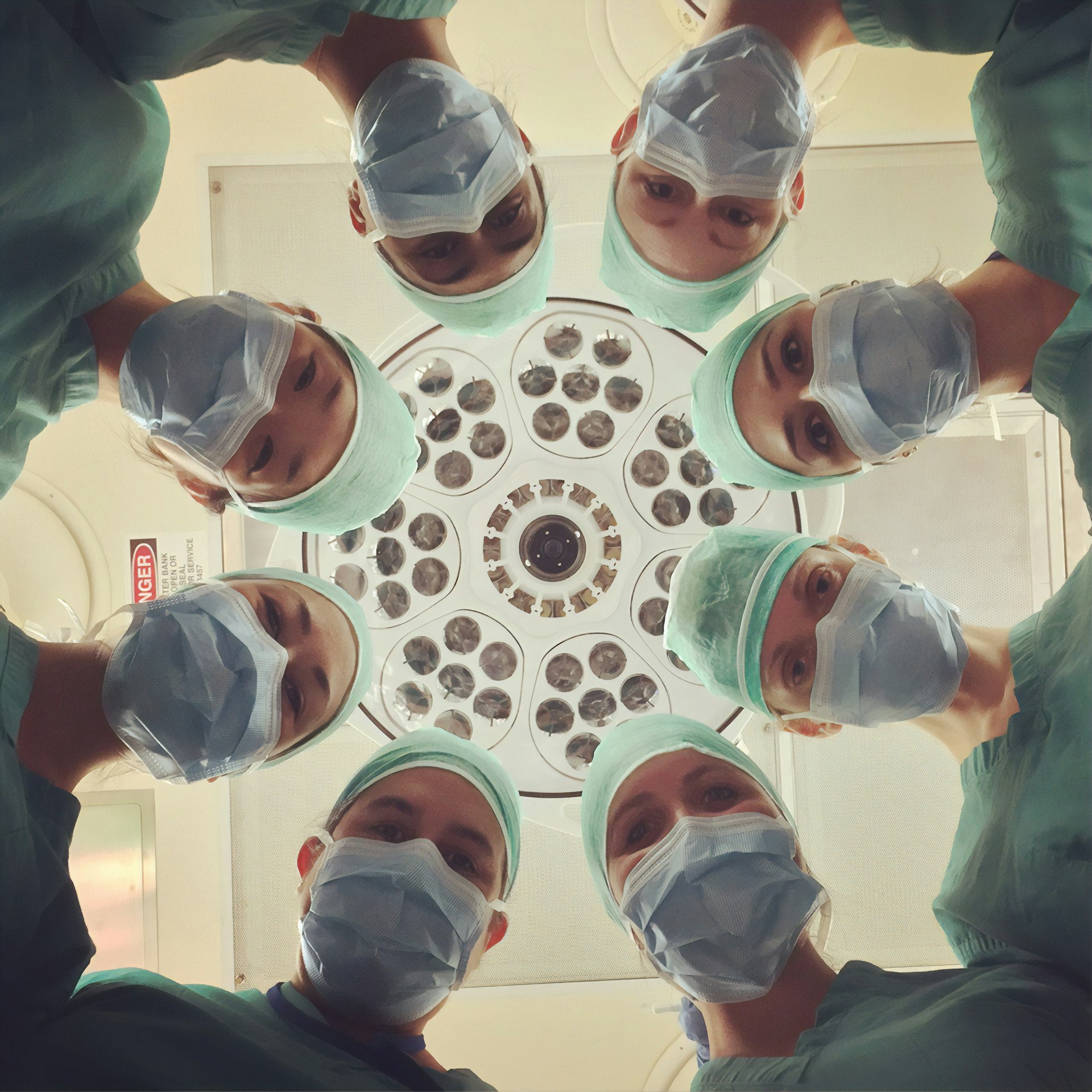 Elysian Health surgical team in green scrubs and masks gathered around a central operating-room light, viewed from the patient's perspective.