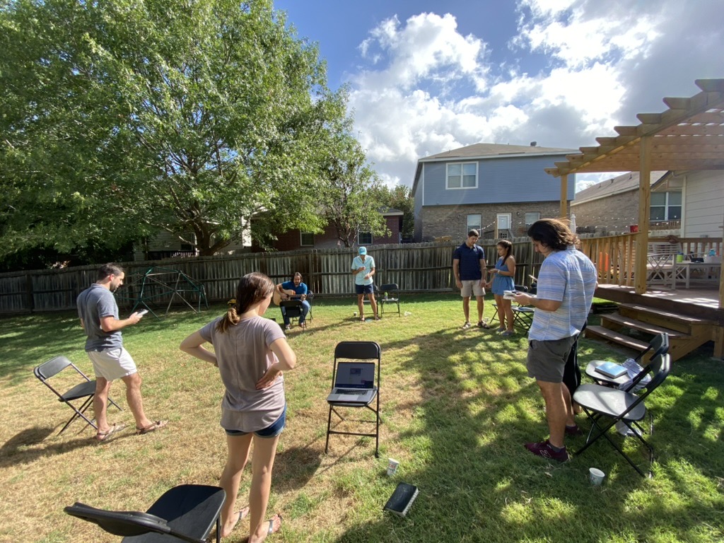 A small group gathered in a circle of folding chairs on a grassy backyard lawn.