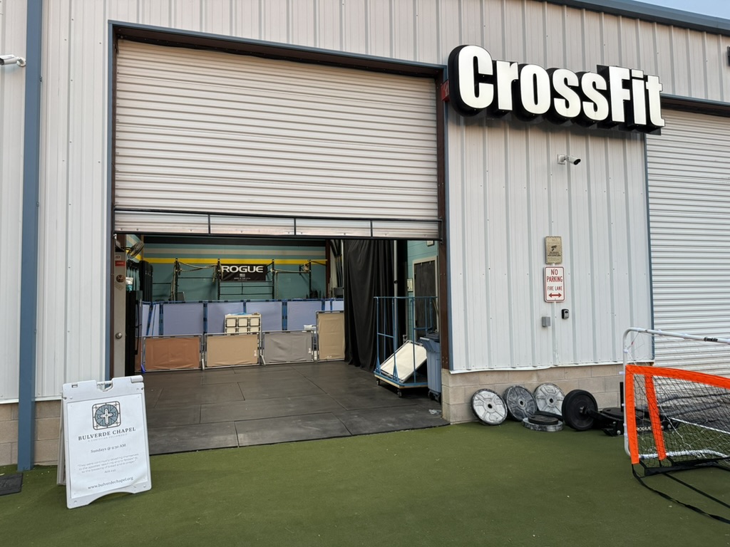 The open bay door of Warrior Park CrossFit, with the Bulverde Chapel sign on the turf outside.