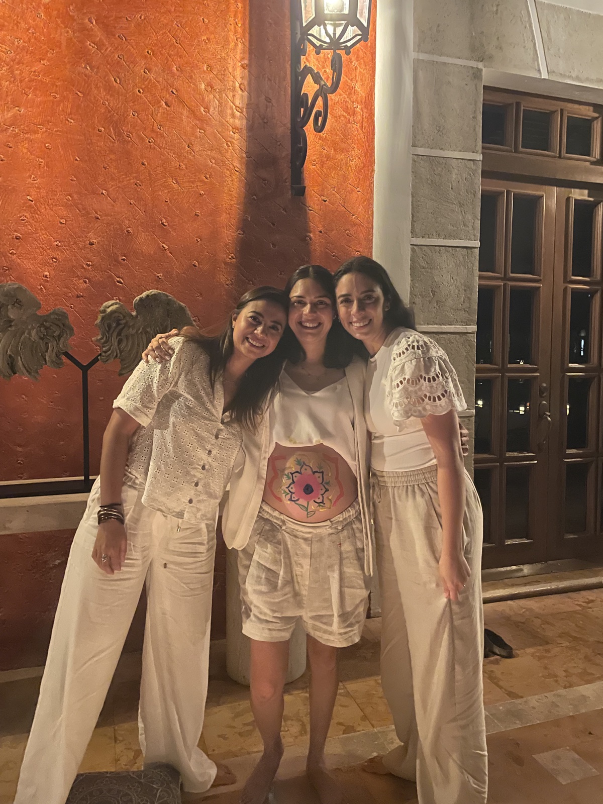Tres mujeres abrazadas en una ceremonia de Blessing Way, una de ellas con un mandala pintado en el vientre embarazado