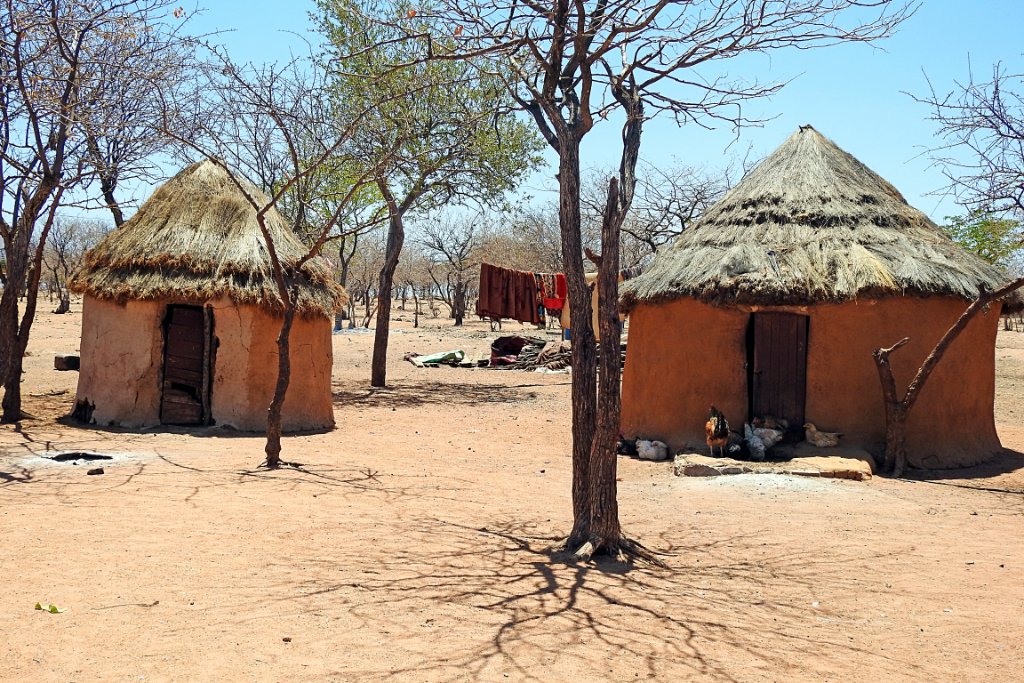 Two traditional thatched huts beside a bare tree in a Himba village in northern Namibia.