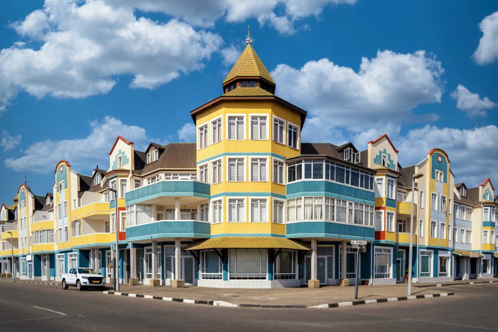 A grand yellow German-colonial building on a street corner in Swakopmund, Namibia, under a bright blue sky.