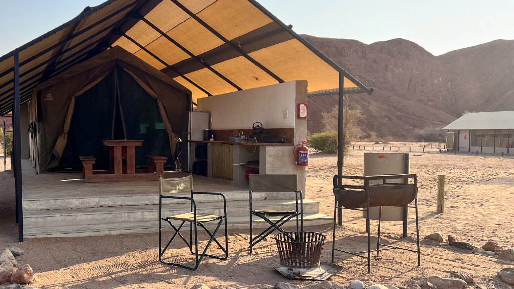 A tented camp with an open kitchen and fire pit set against red desert hills in Namibia.