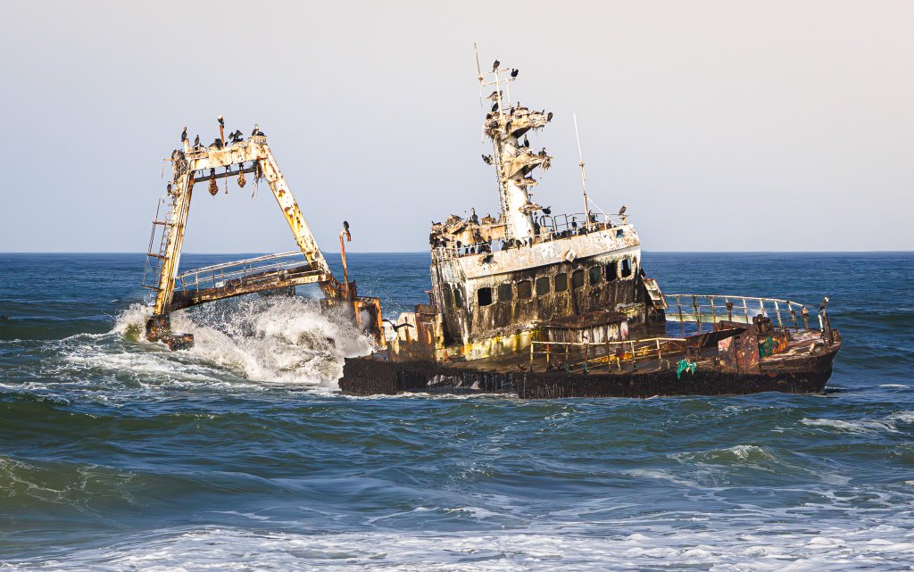 A rusting shipwreck lists in the surf along Namibia's Skeleton Coast, waves breaking around its weathered hull.