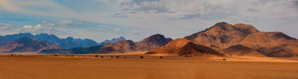 Red sand dunes and desert mountains rising over a wide Namibian gravel plain under an open sky.