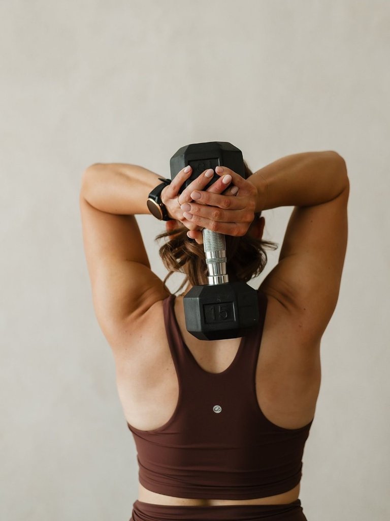 A woman performing an overhead dumbbell extension during a strength session