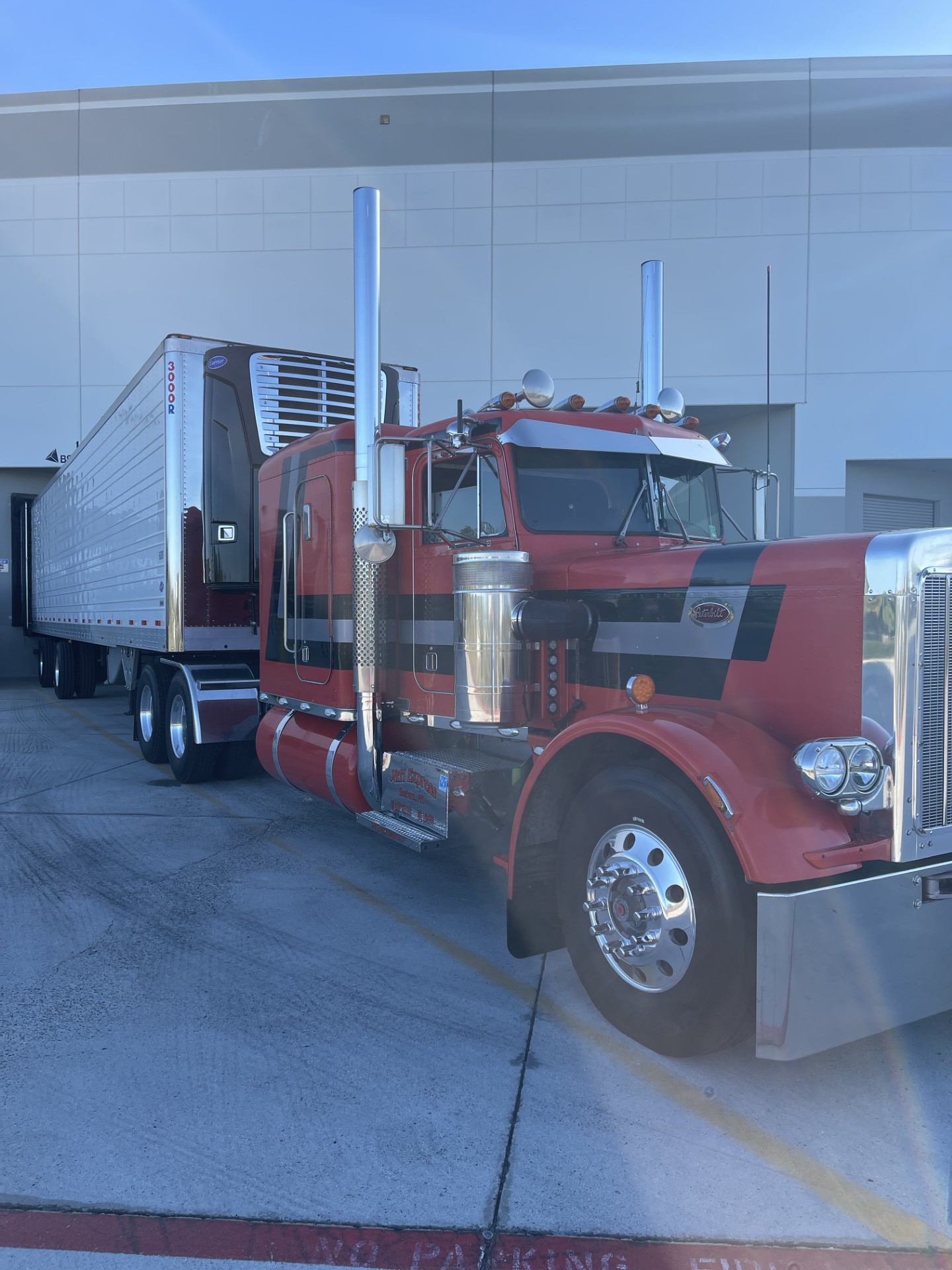 Red and black Peterbilt with a white refrigerated trailer at the dock