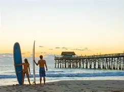 Surfers with boards on a Space Coast beach at golden hour