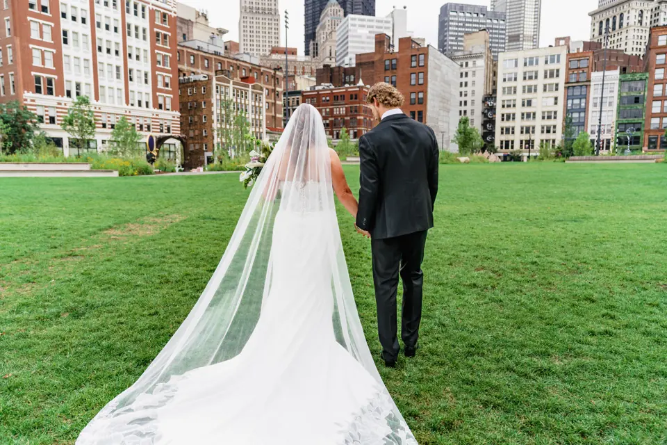 Bride's long veil trailing across a lawn toward the Pittsburgh skyline