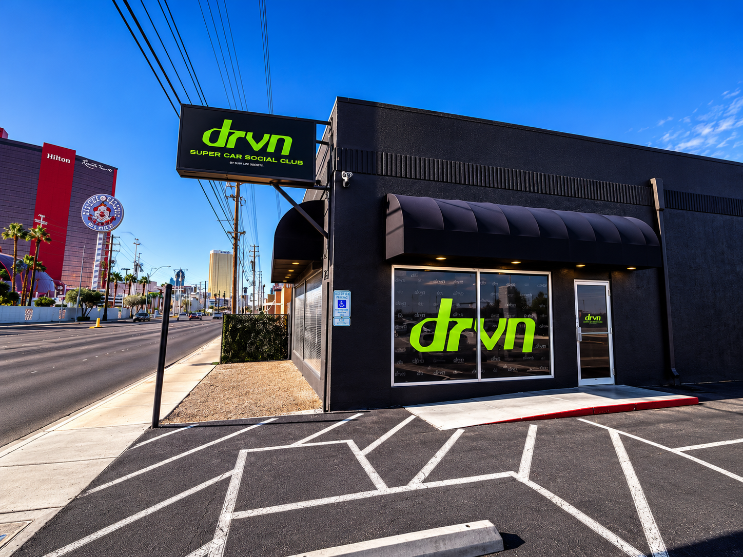 Black DRVN storefront with a lit sign and window logo, with the Las Vegas Strip in the background