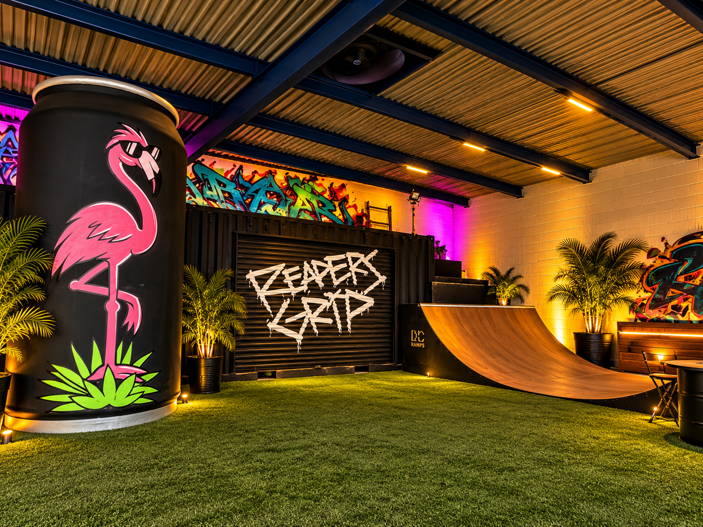 Paddock flamingo artwork beside a mural shutter and a wooden skate ramp on artificial turf