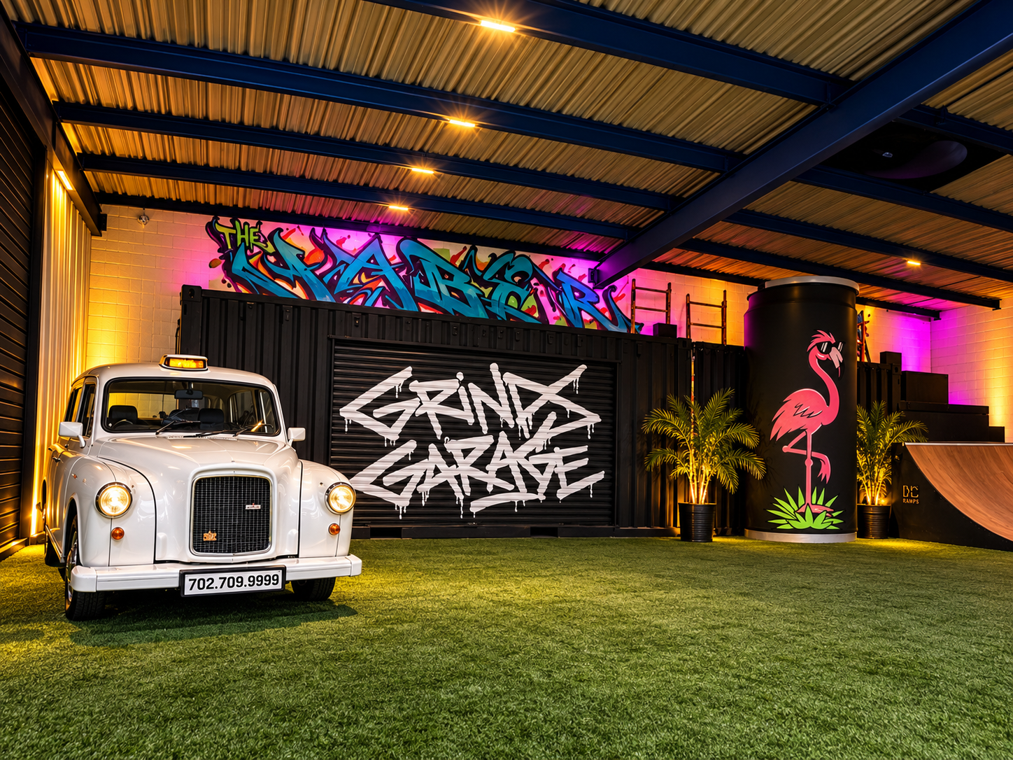 White taxi in the covered Paddock in front of a Grinds Garage mural and a flamingo artwork