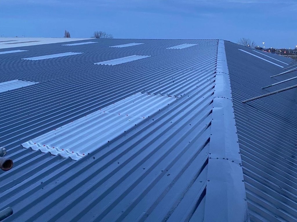 Metal roof coating completed at dusk — dark graphite TopSpray35 finish across corrugated metal roof with rooflight panels visible