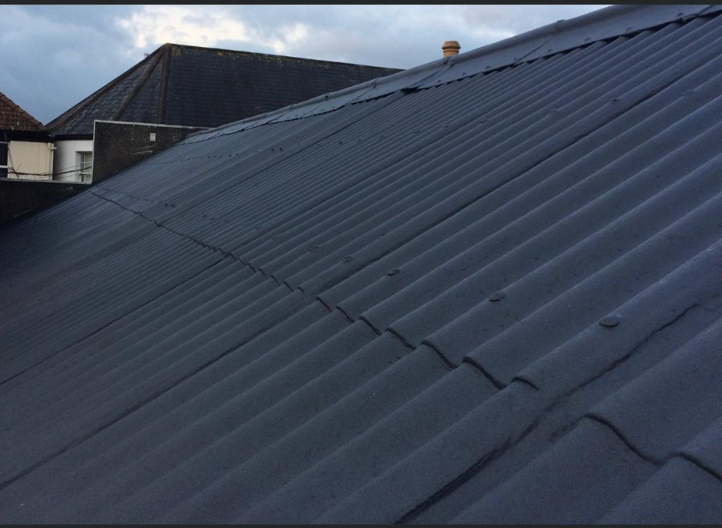 Pitched corrugated metal roof — completed TopSpray35 coating, grey finish across full pitched surface, red brick building
