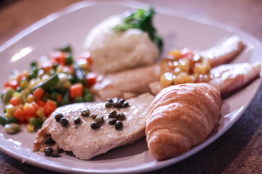 Plated dinner of chicken breast, mashed potatoes, vegetables, and a warm roll