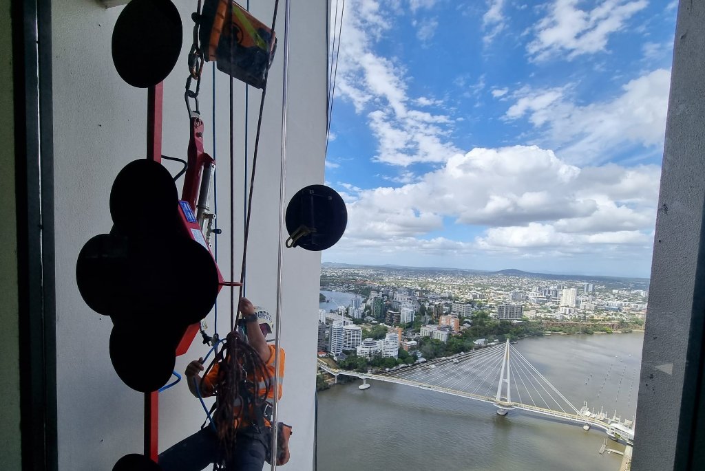 Technician using glass sucker at height with Brisbane city view