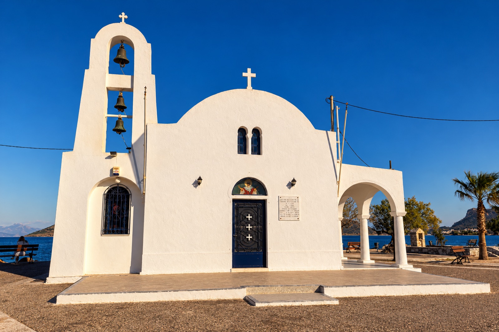 White seaside chapel with bell tower and palm trees on the Porto Rafti waterfront
