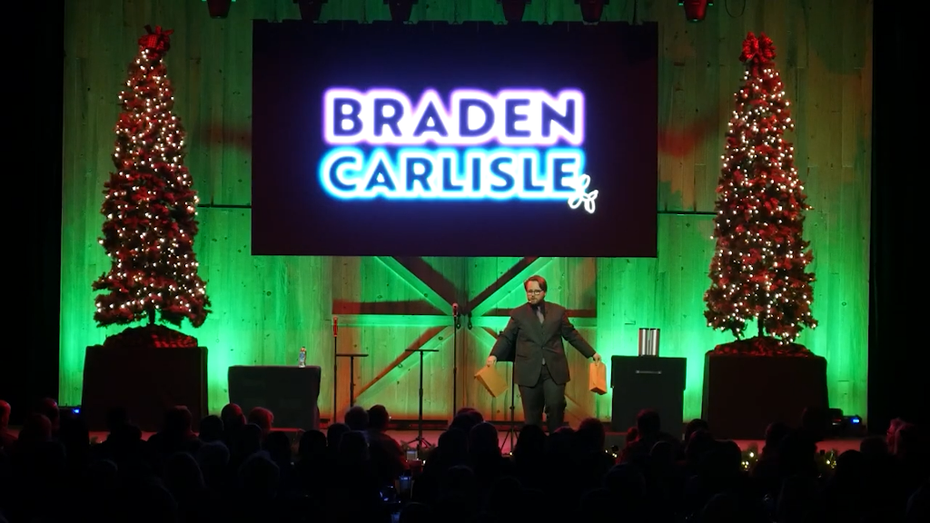 Braden Carlisle on stage at a holiday party with neon name backdrop