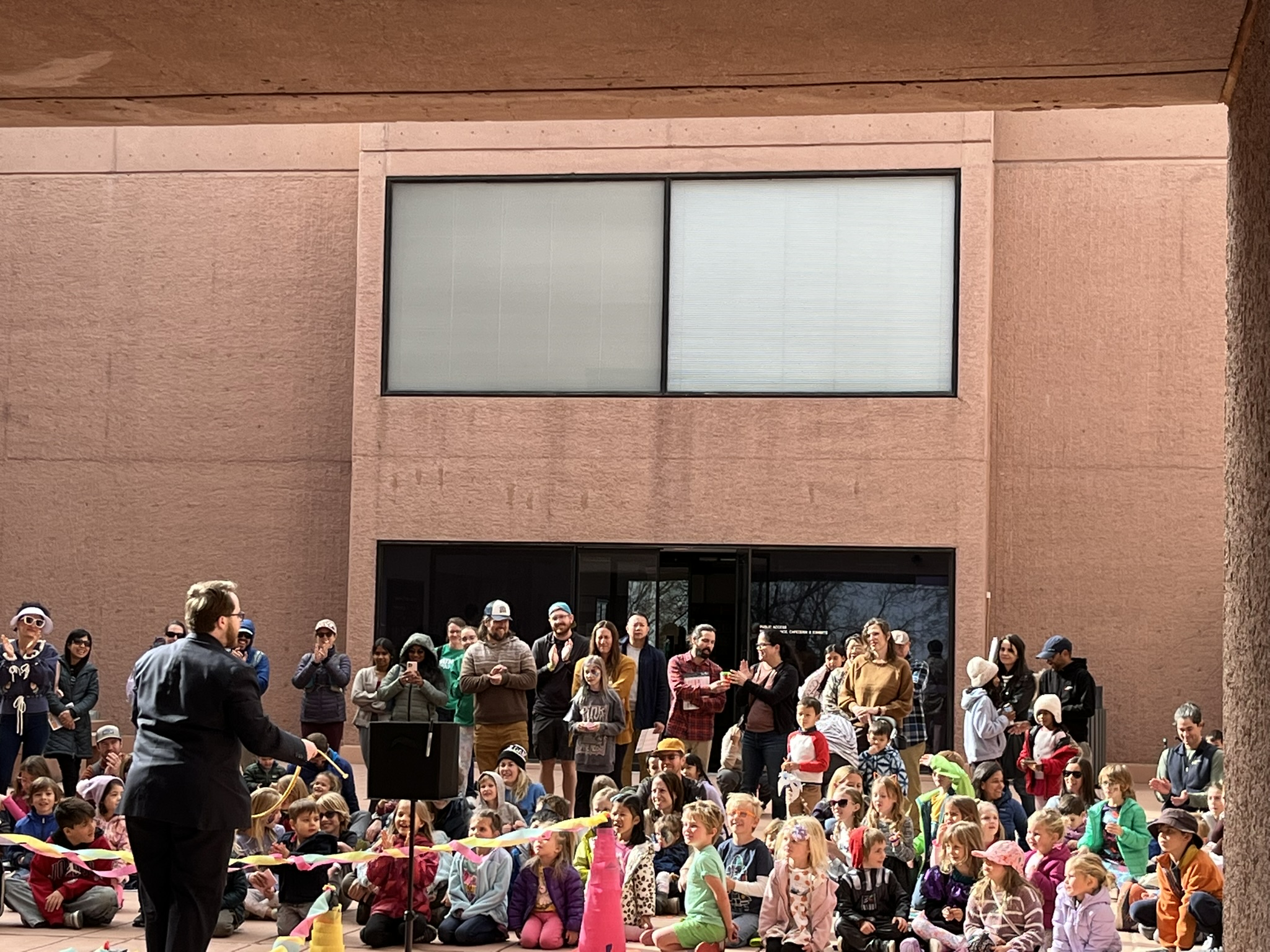 Braden Carlisle performing a magic show for a crowd of kids and parents in an outdoor courtyard