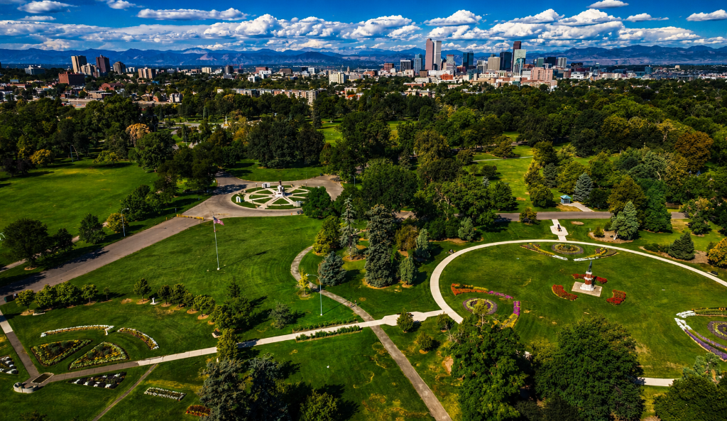 City Park Denver aerial — lush green park with flower gardens, Denver skyline and Rocky Mountains in background