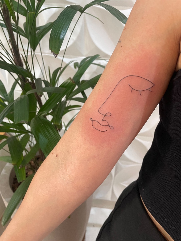 Minimalist face line art tattoo on forearm