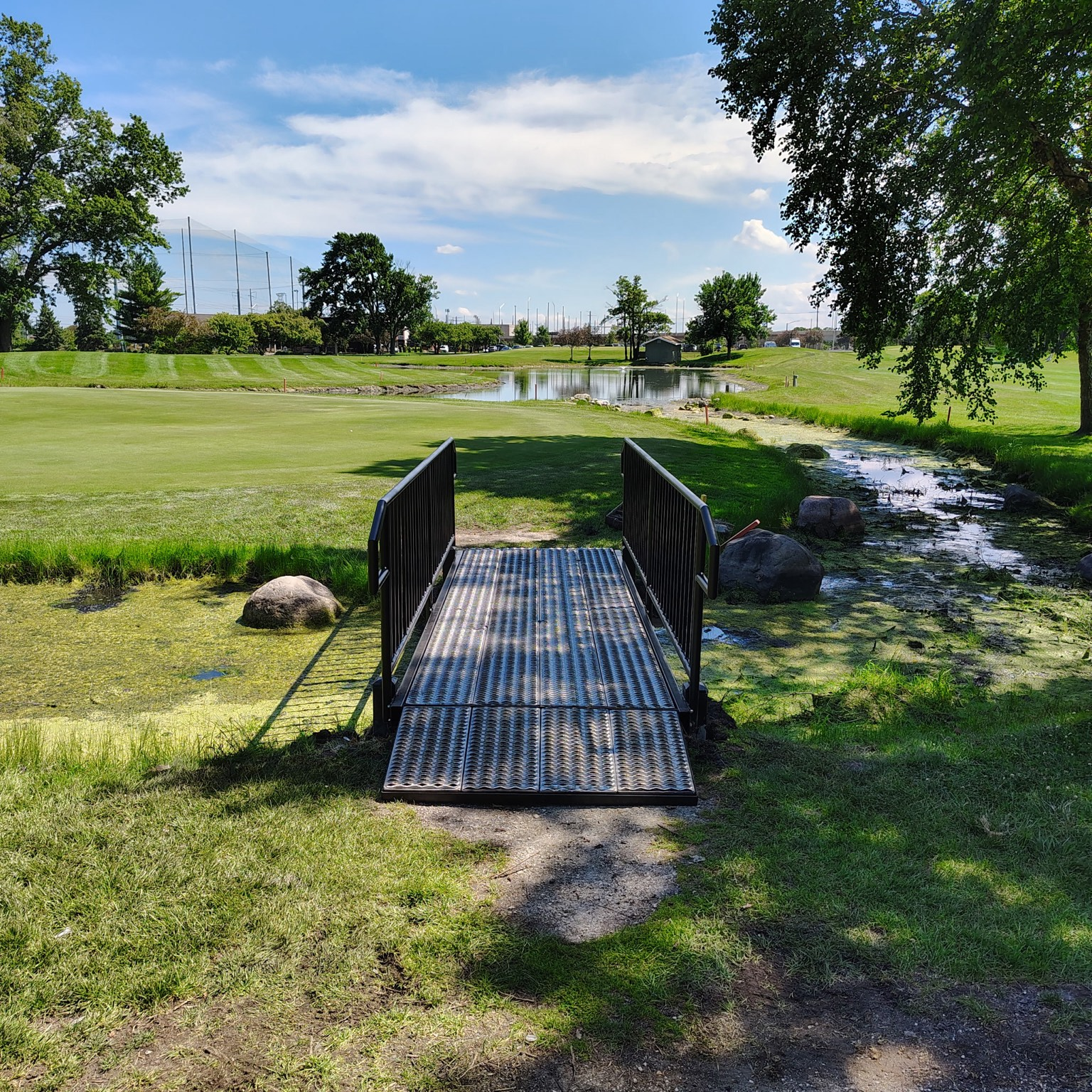 Small steel pedestrian bridge with an expanded-metal deck spanning a creek.