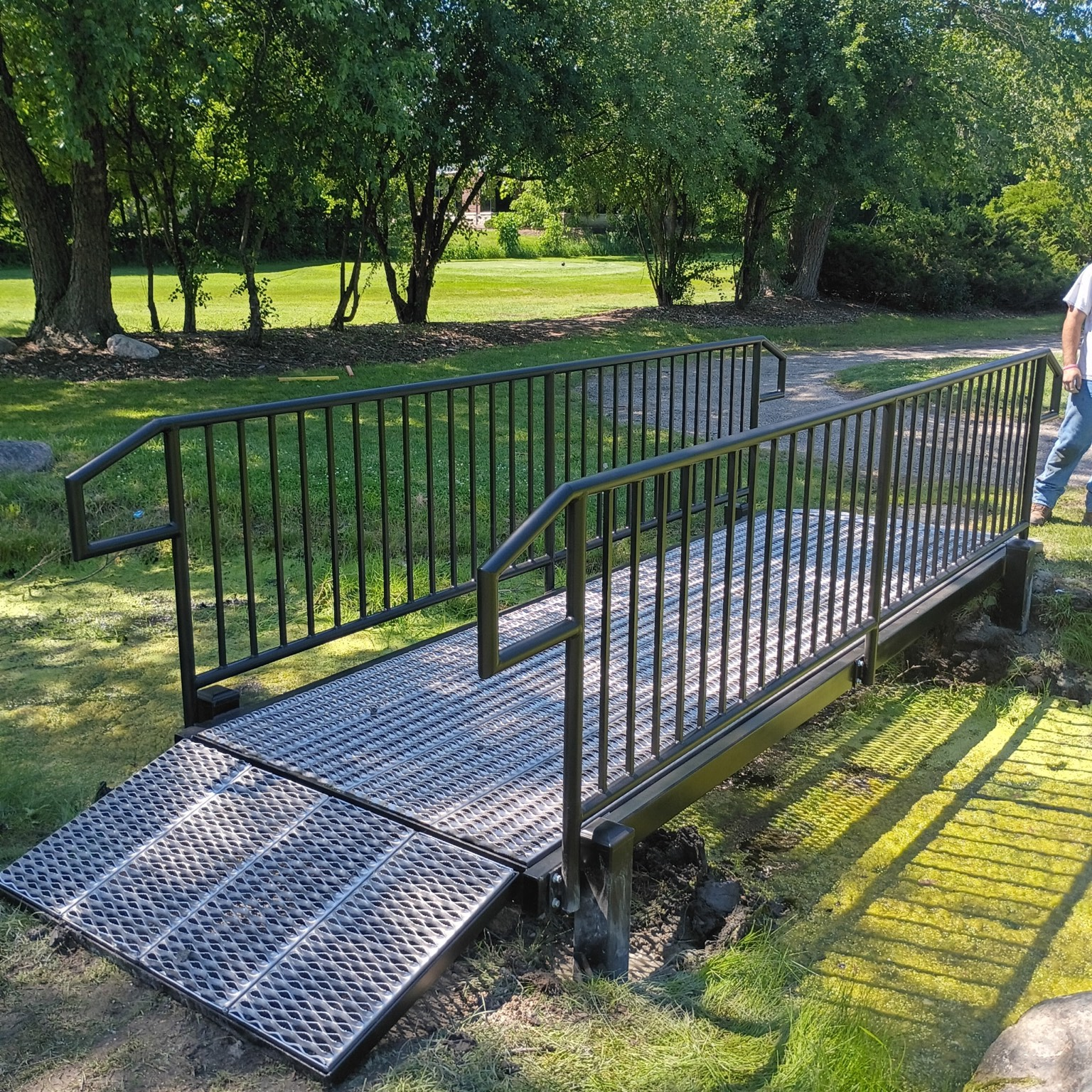Completed custom pedestrian bridge with integrated metal railings and grated walking surface at a golf-course property.