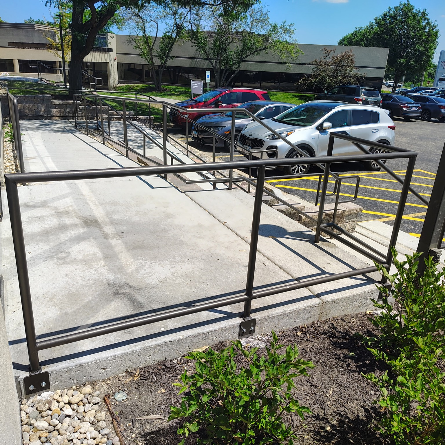 Metal handrail and mid-rail system installed along a concrete access ramp.