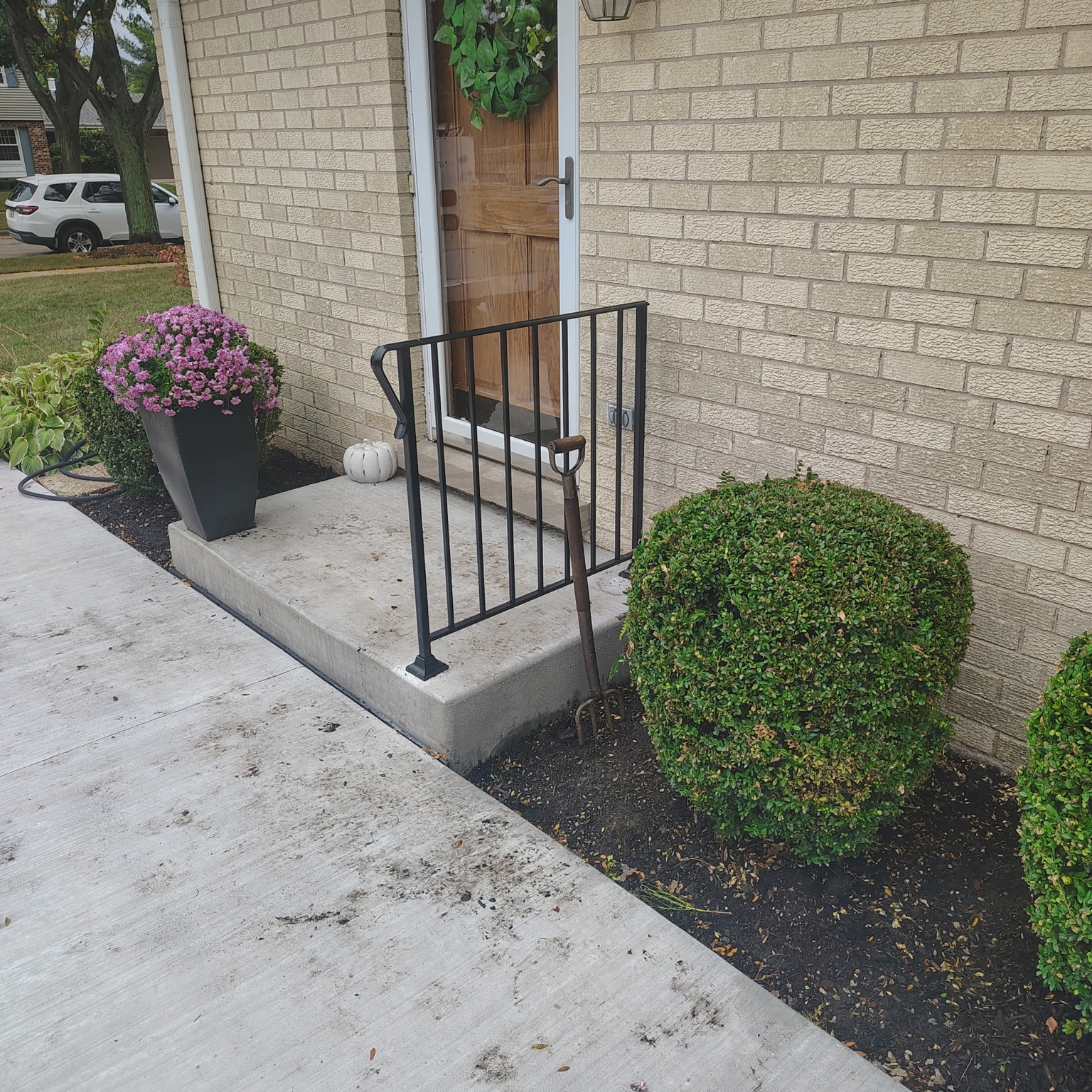 Black metal handrail with a curved top rail on concrete steps at a brick home.
